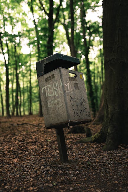 An outdoor scene showcasing scattered debris and packaging materials on a patch of grass and dirt at the edge of a dirt slope. The debris includes flattened cardboard boxes, many with green and white